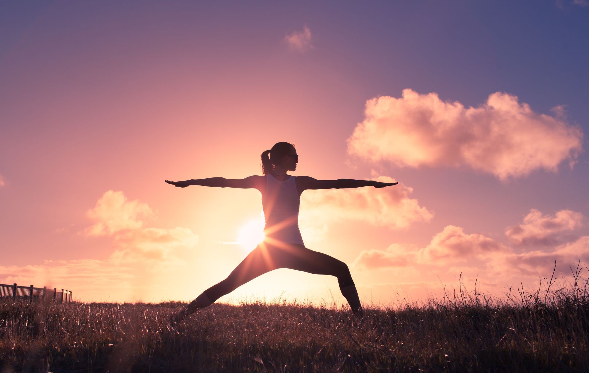 Person doing a warrior yoga pose at sunset in a field