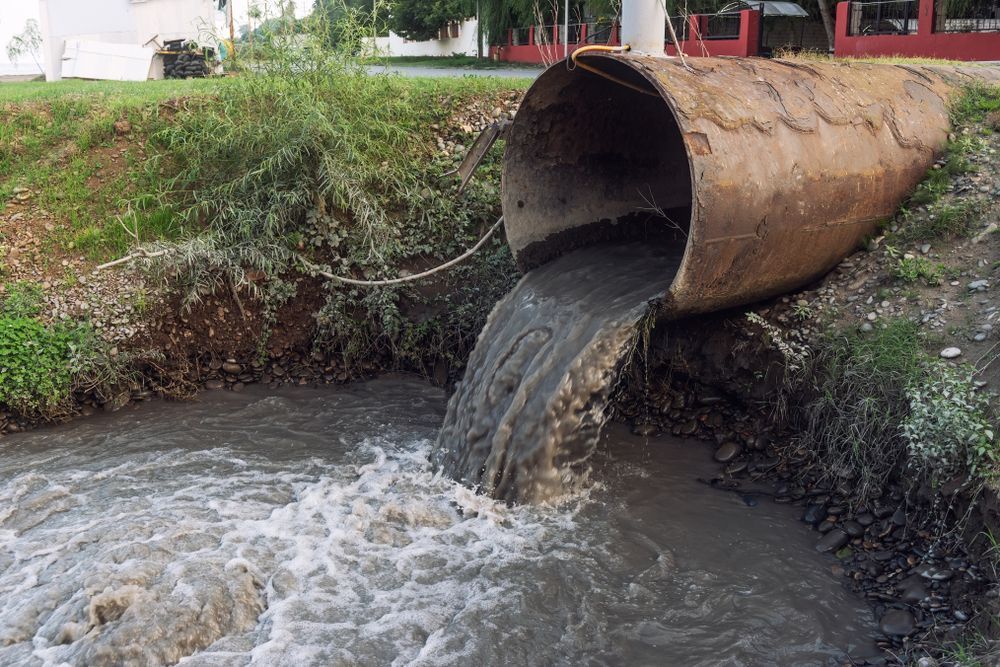 A Large Pipe is Pouring Dirty Water Into a River — Hoges Plumbing In West Wollongong, NSW