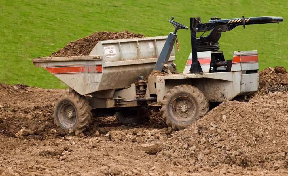 A Dump Truck is Driving Through a Dirt Field — Hoges Plumbing In Shellharbour, NSW
