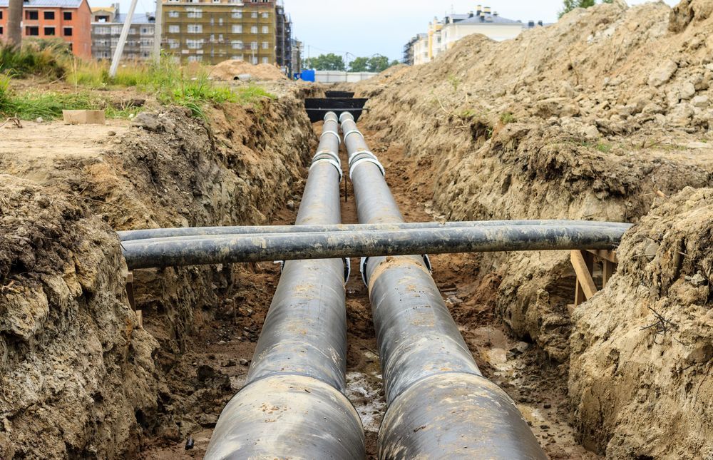 Two Pipes Are Being Installed in a Trench in the Dirt — Hoges Plumbing In West Wollongong, NSW