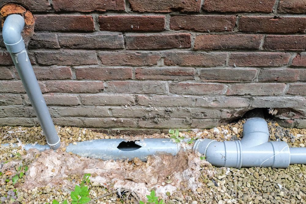 A Pipe With a Hole in It is Sitting Next to a Brick Wall — Hoges Plumbing In Helensburgh, NSW