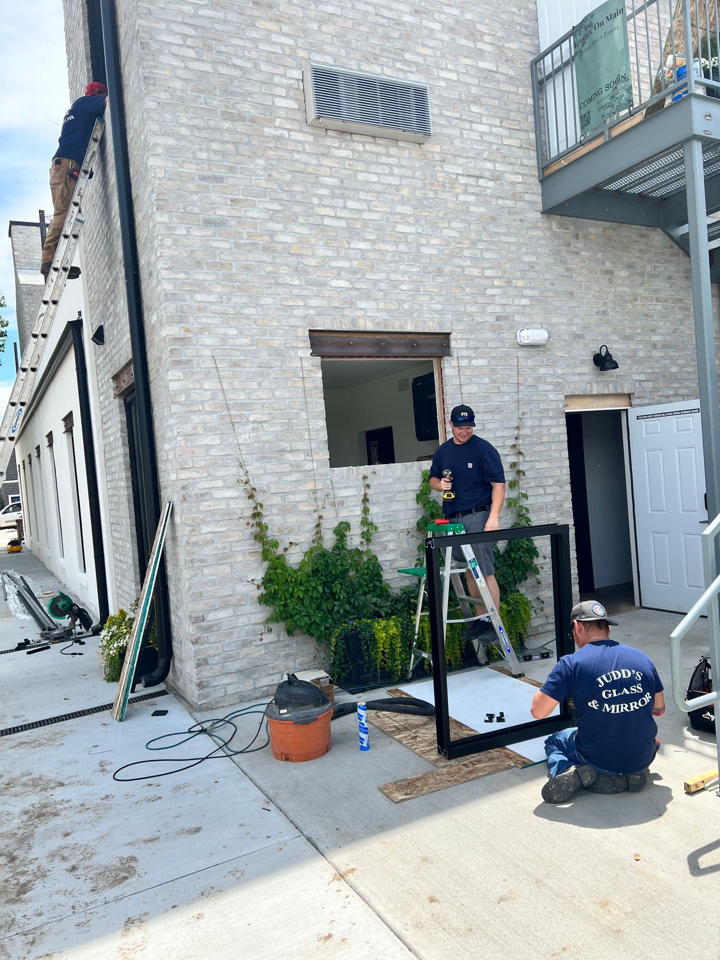 Two men are working on a window on the side of a building.