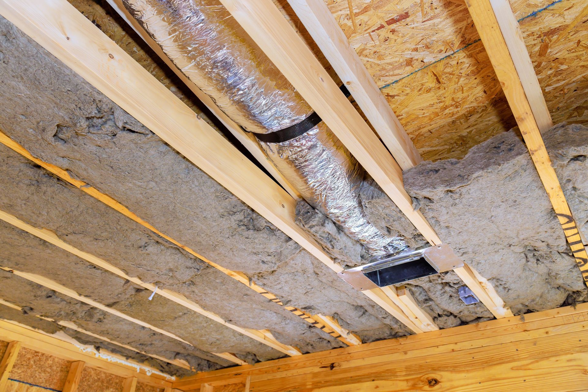 Basement ceiling with exposed insulation, wood joists, and silver ductwork under construction