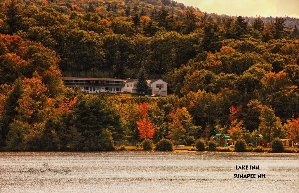 Autumn foliage surrounds a lakeside motel, colorful trees on a hillside.