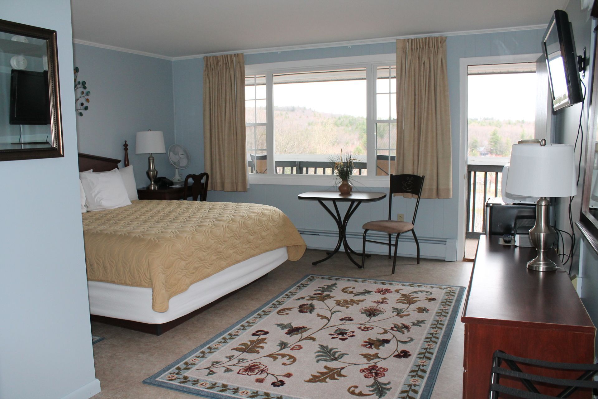 Bedroom with bed, rug, table, chair, window with view, and open door to balcony.