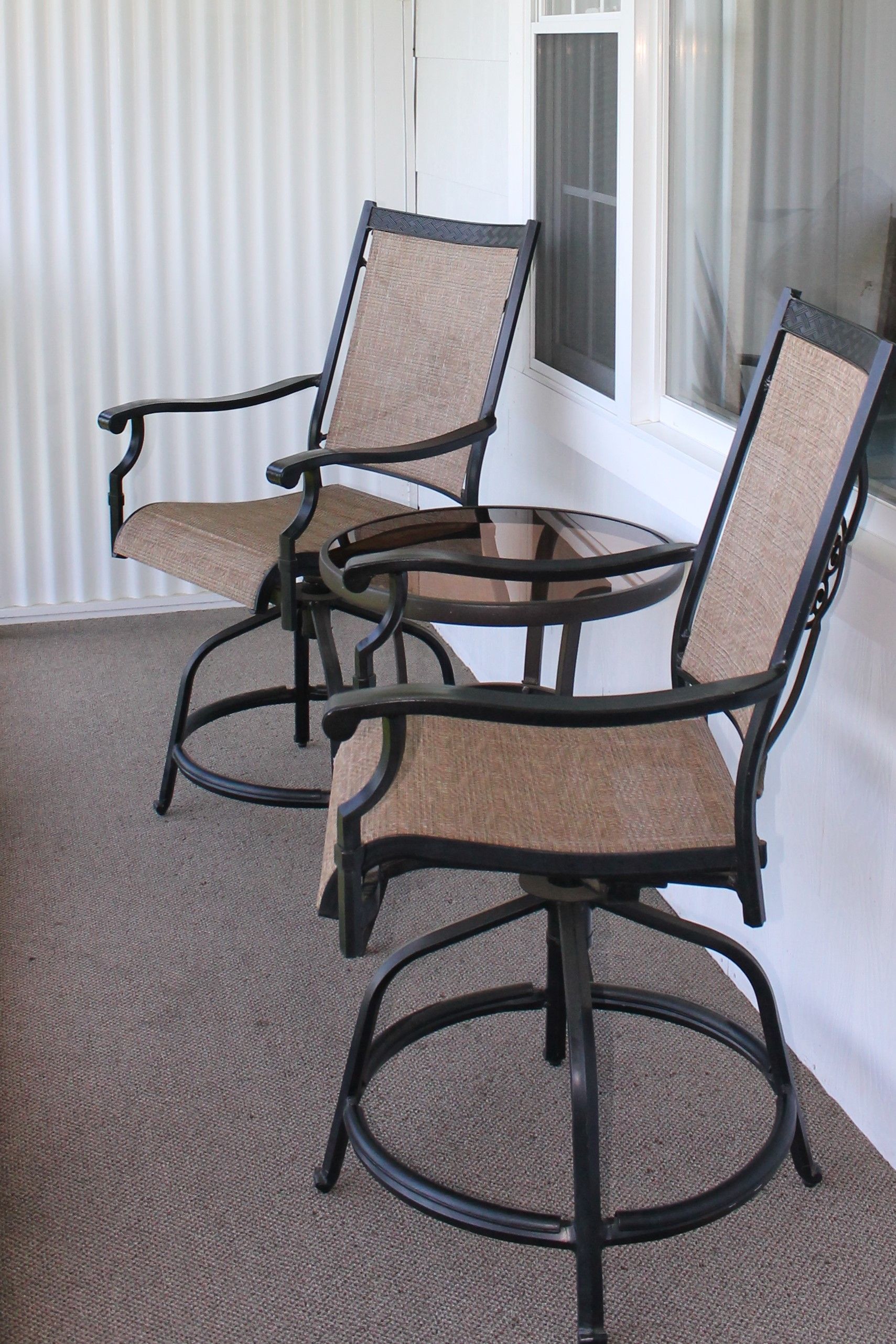Two black metal chairs and a small table on a porch, neutral colors.