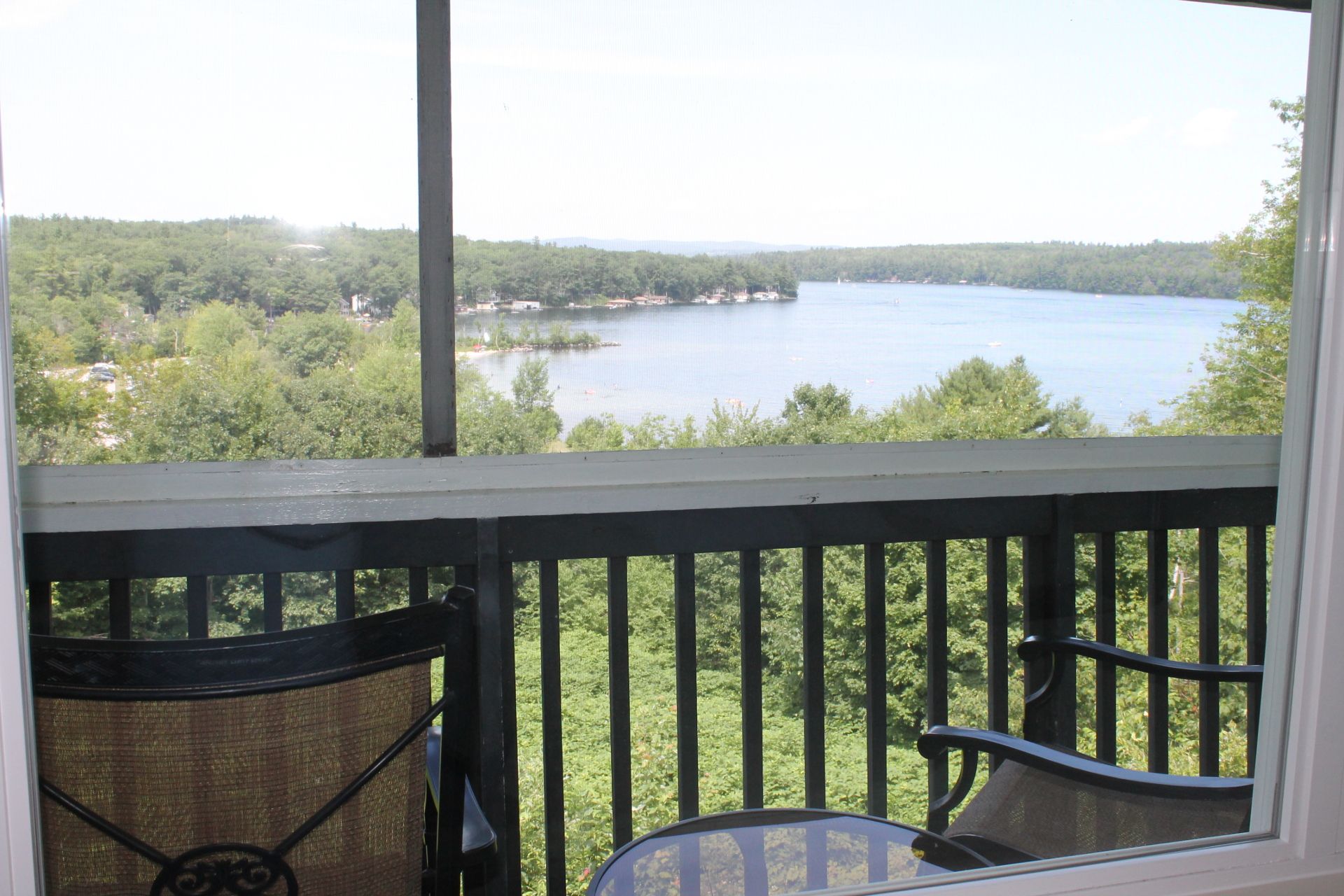 View of a lake from a screened porch, with trees and homes along the shore.
