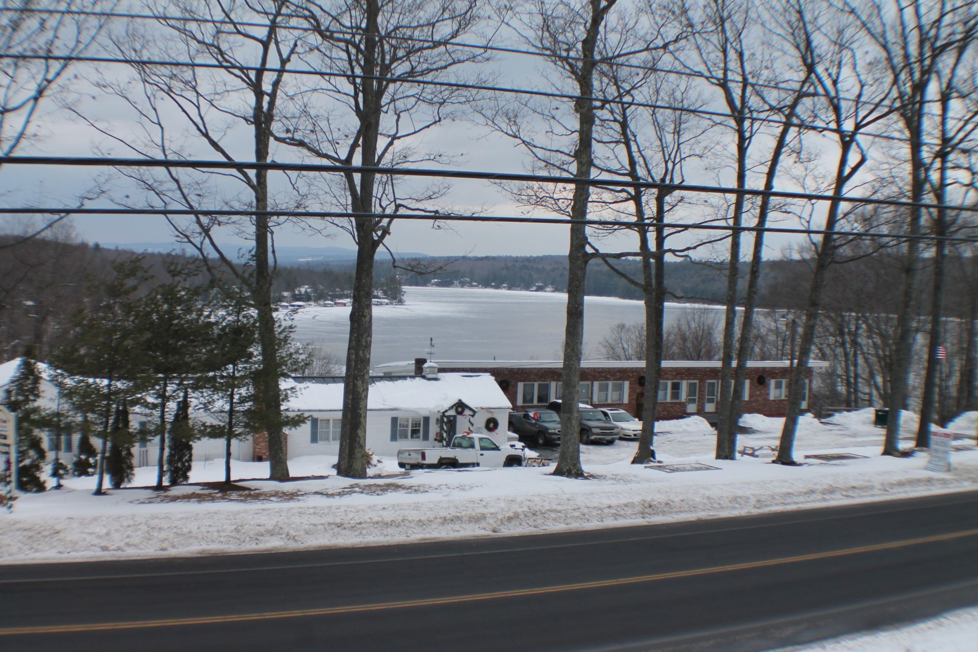 Snowy lake view with trees, motel, and road.