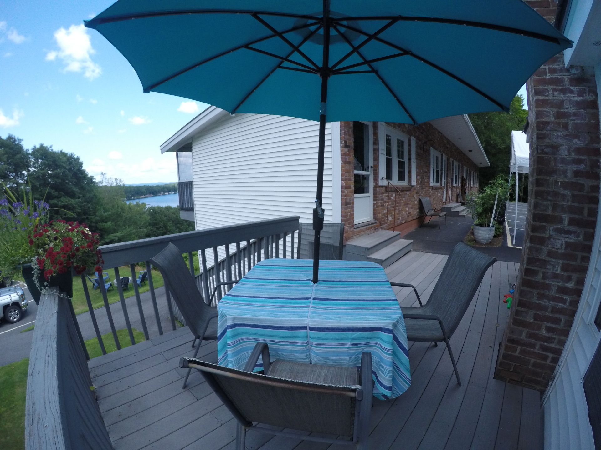 Blue umbrella over a table with chairs on a wooden deck overlooking a lake.