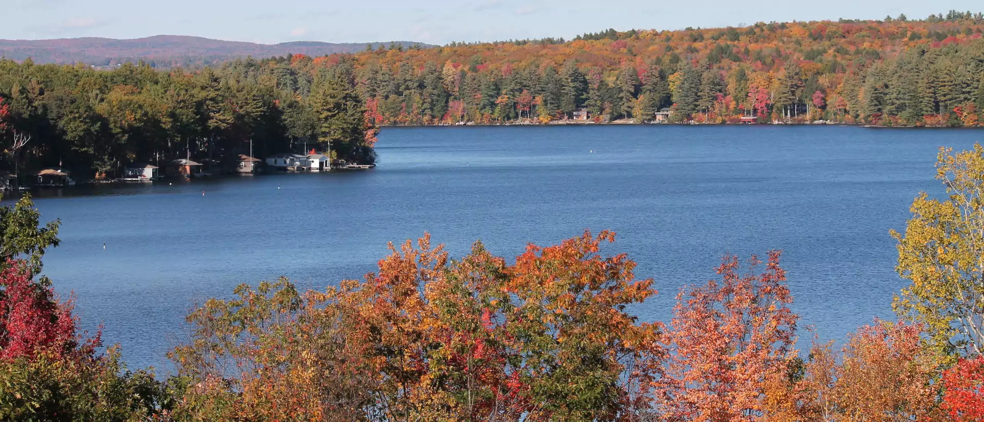 Lake surrounded by trees with autumn foliage. Bright blue water, clear sky.