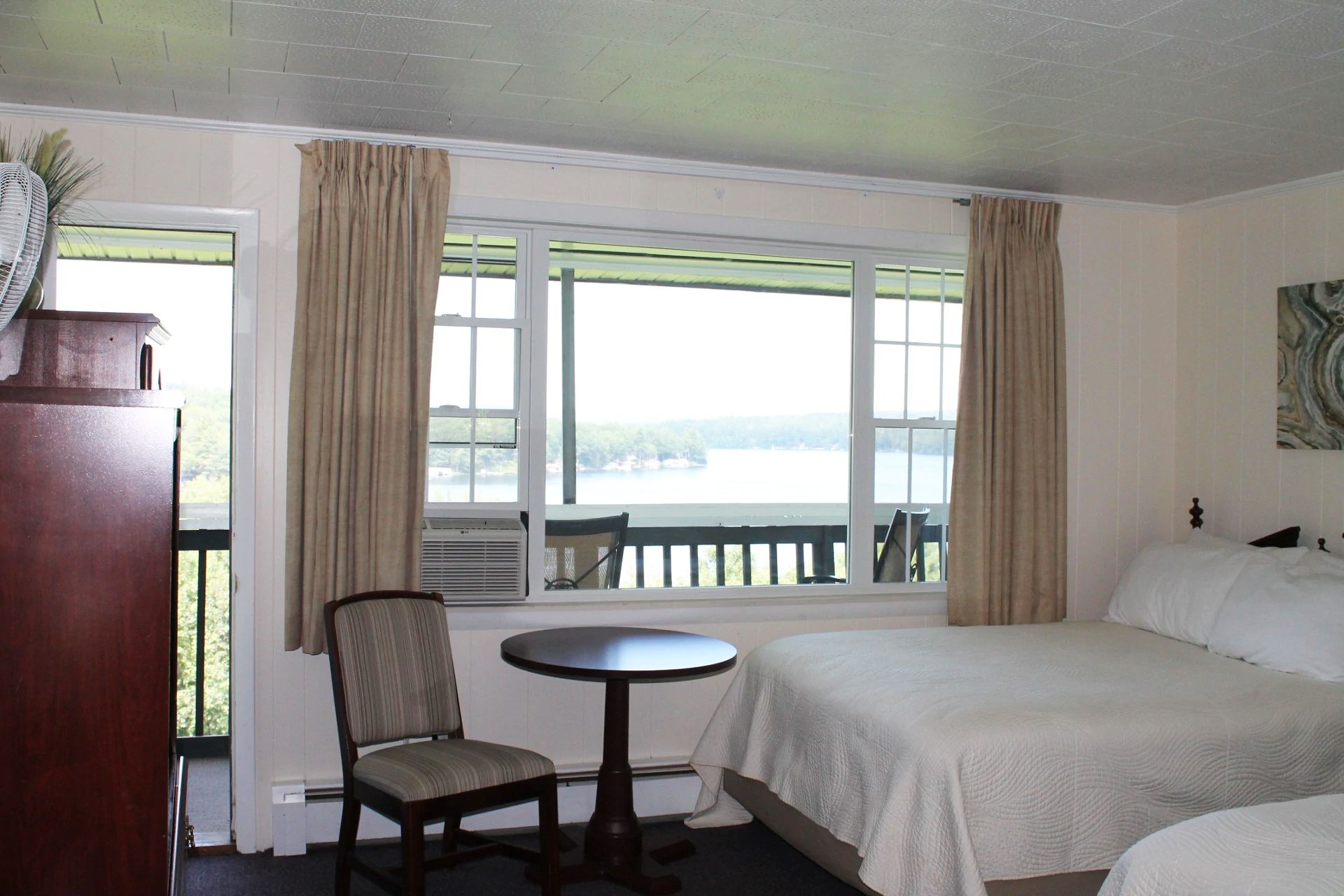Hotel room with two beds, a table, and a balcony view of a lake.