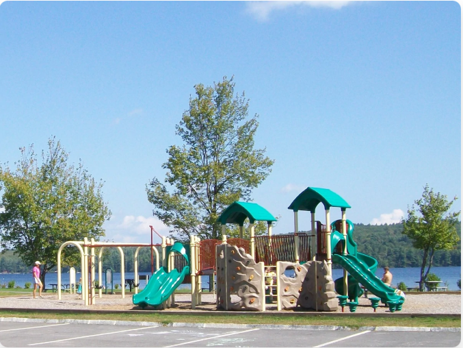 Playground with slides and swings near a lake on a sunny day.