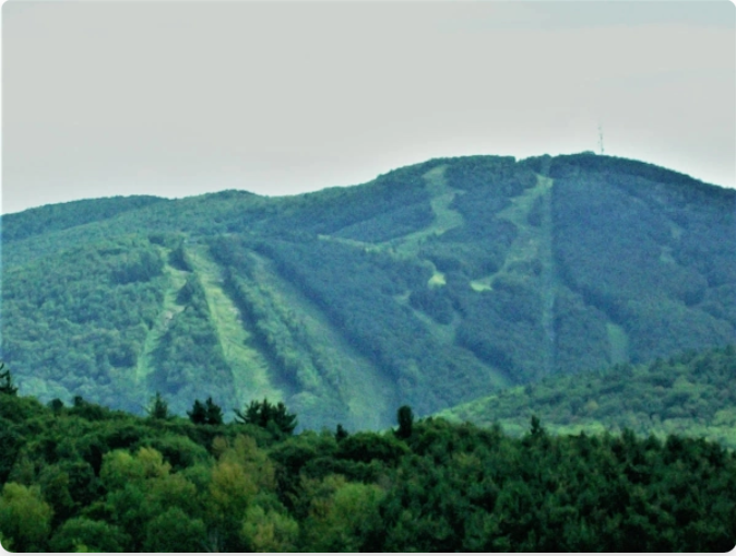 Green mountain with ski runs cut through trees, antenna tower on the peak.