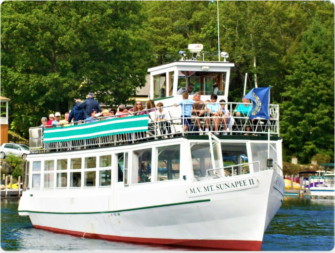 A white tour boat with passengers on a lake, green trees in the background.