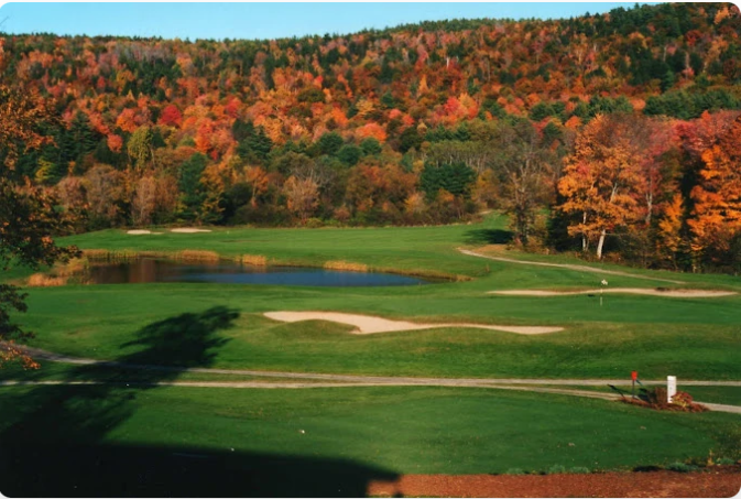 Golf course in autumn. Green fairways, water hazard, sand traps, trees with red and orange foliage.
