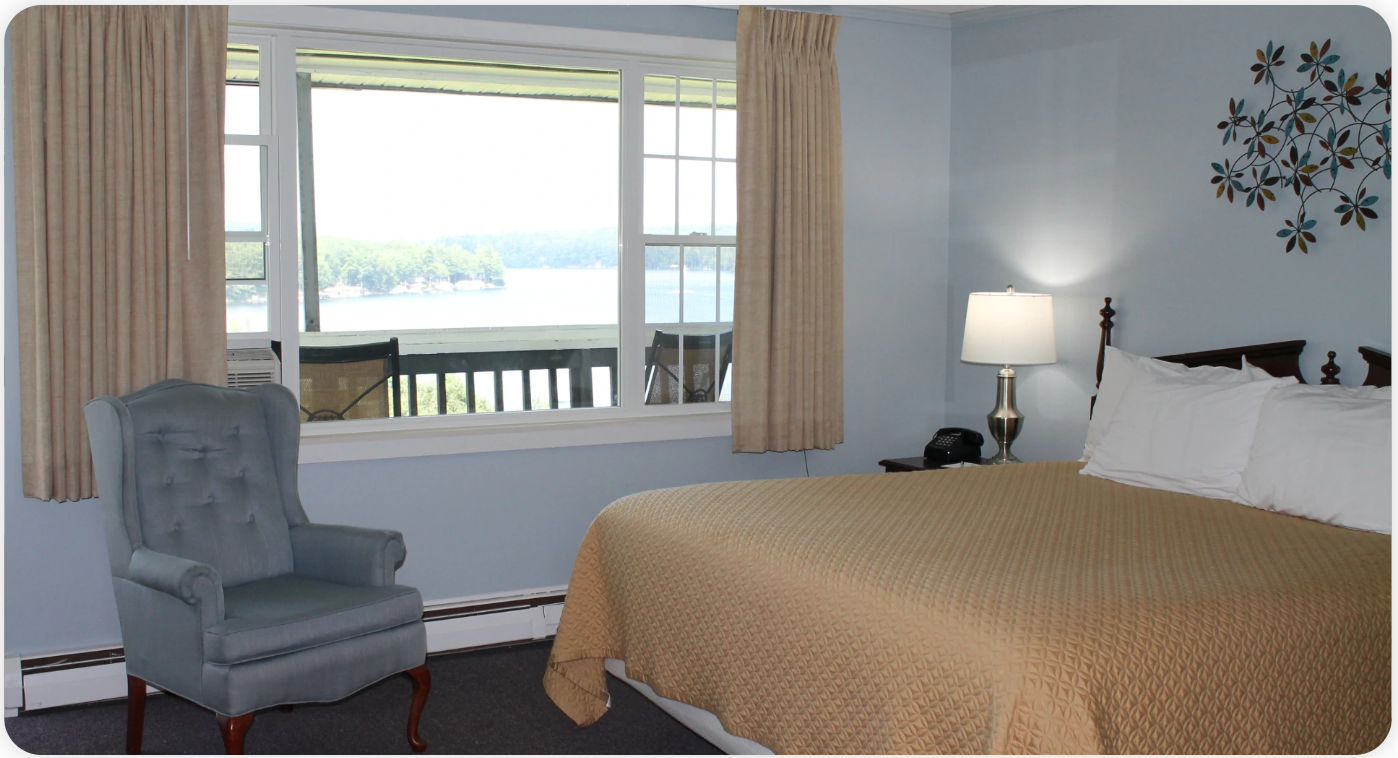 Bedroom with blue walls, bed, chair, window overlooking water.