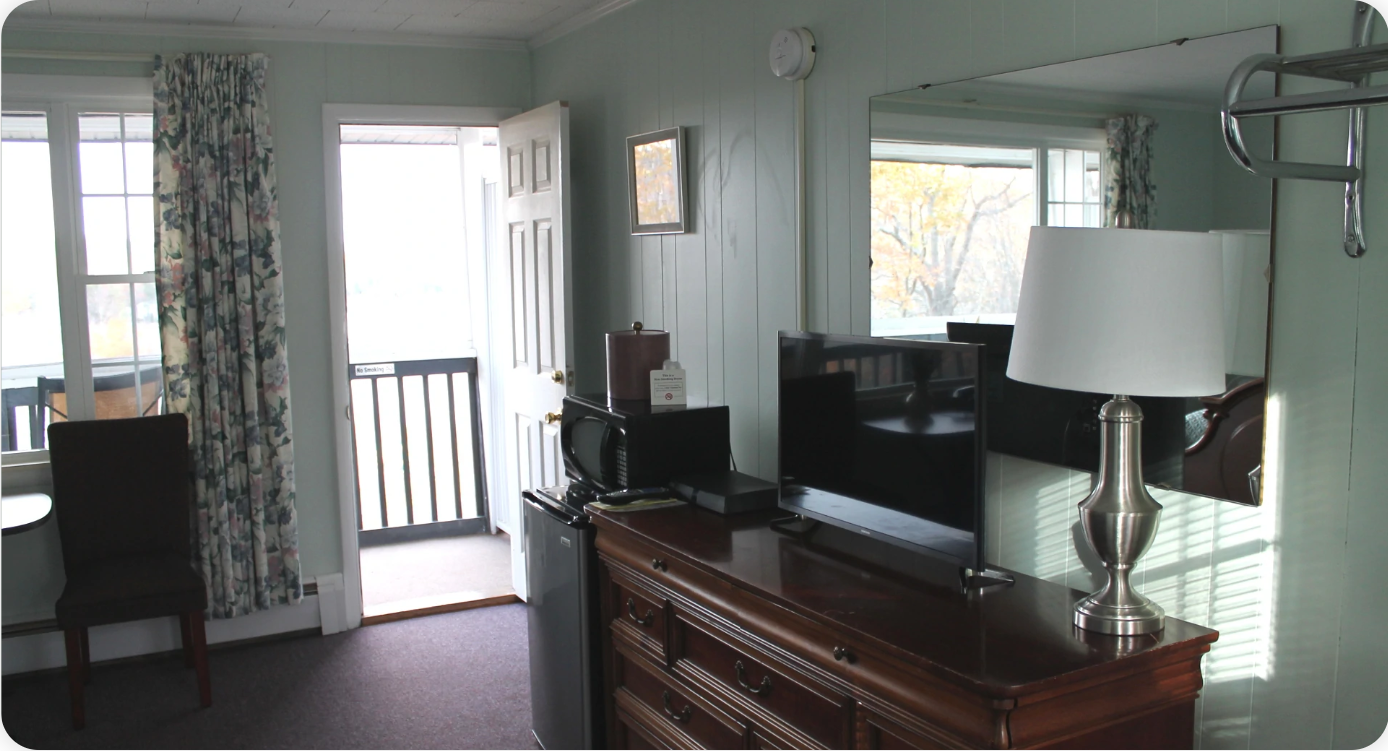 Hotel room interior with a door to a balcony, dresser, mirror, TV, microwave, and chair.