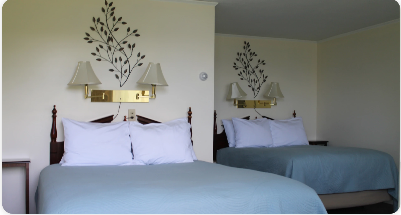 Two beds in a room with a decorative branch design on the wall, beige walls, and matching lamps.