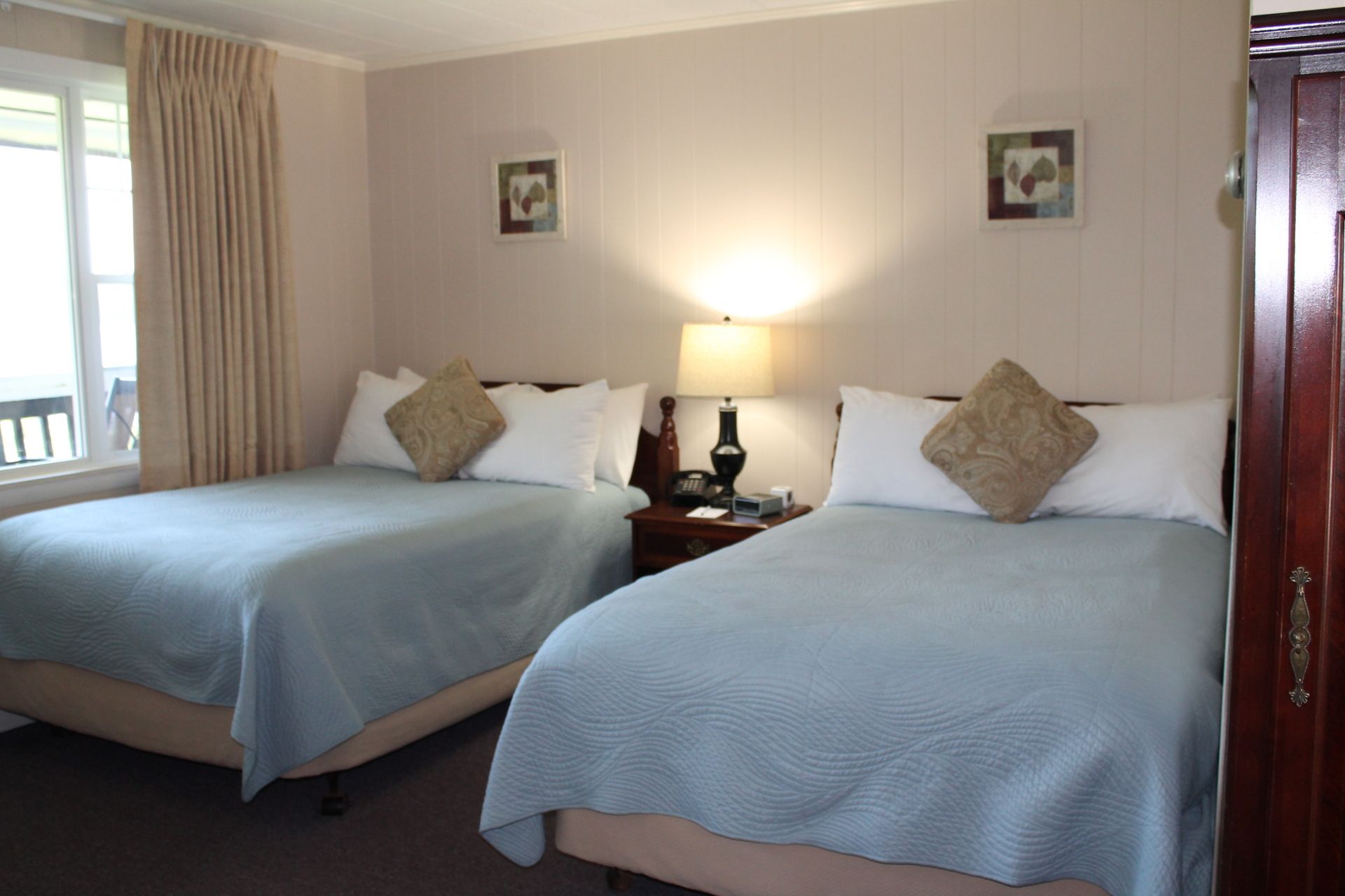 Two beds in a hotel room with light blue bedspreads, neutral walls, and a window.