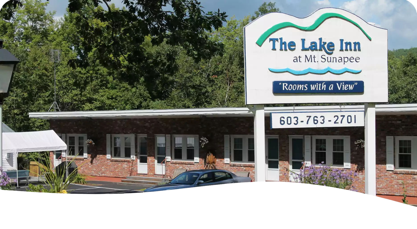 The Lake Inn at Sunapee motel exterior with sign, brick facade, and car parked out front.