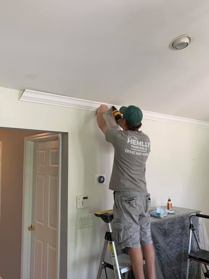 Worker installing crown molding on a ceiling in a room with a door and step ladder.