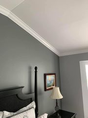 Gray bedroom corner with black headboard, bedside lamp, and framed painting on the wall