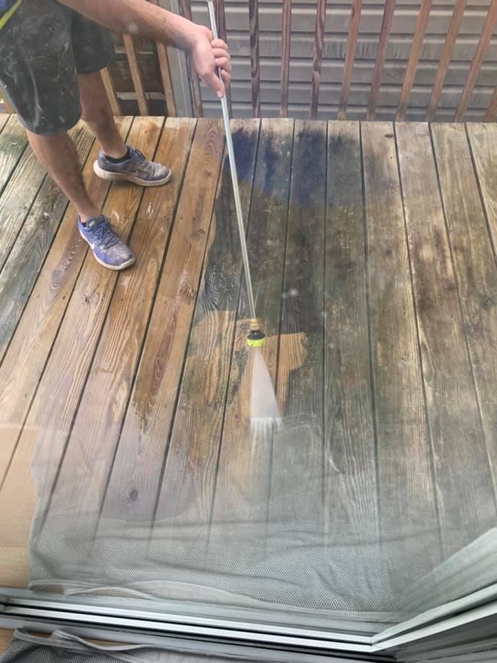 Person pressure-washing a wooden deck, spraying water onto weathered boards near a railing.