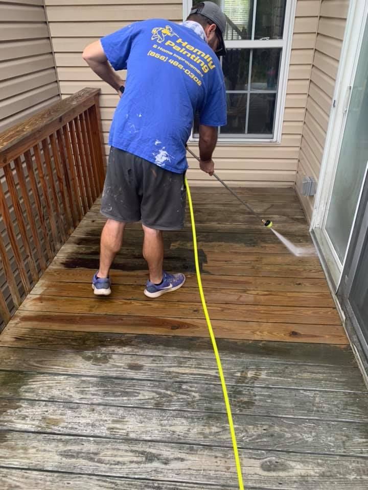 Worker power-washing a wooden deck beside a house.