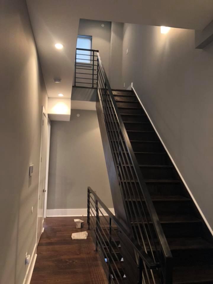 Indoor stairwell with black metal stairs and railing, gray walls, and wall lights leading to an upper landing
