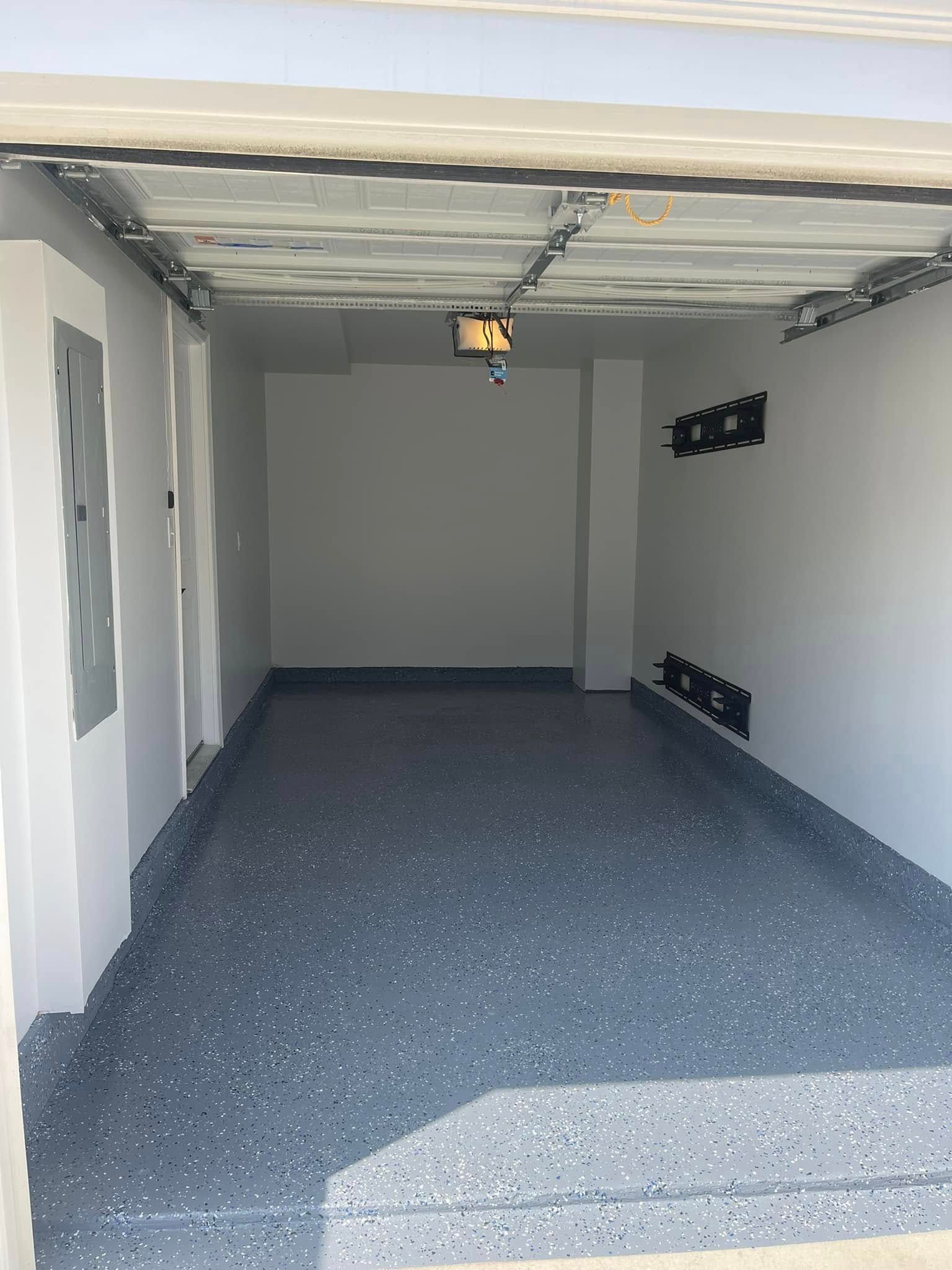 Empty garage with gray speckled floor, white walls, and an unfinished ceiling.