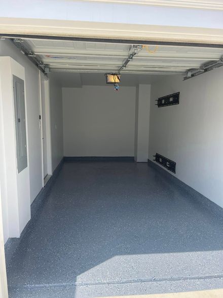 Empty garage with speckled gray floor, open ceiling, and a raised step at the front.