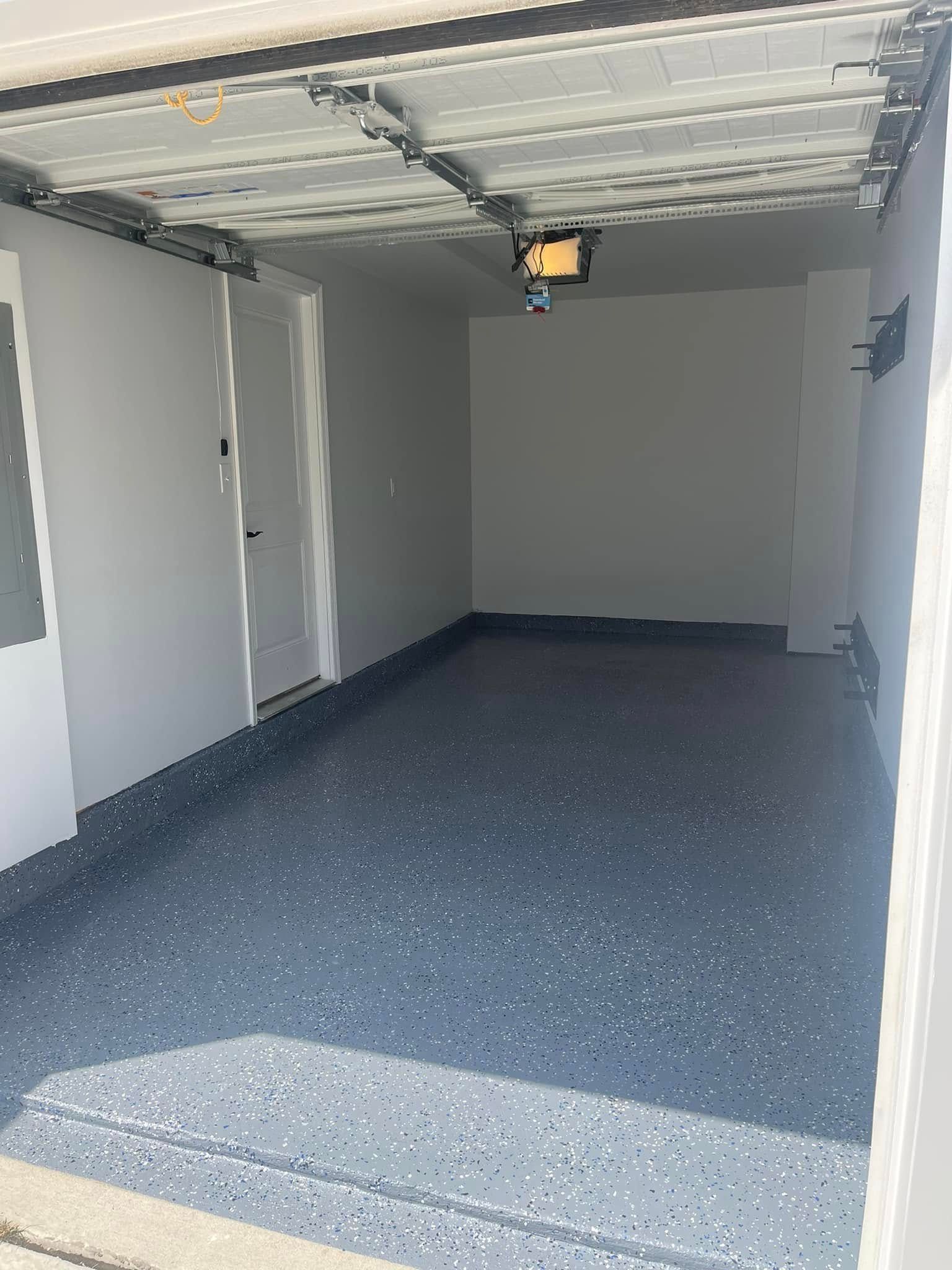 Empty gray garage with speckled floor and overhead door open, lit by daylight