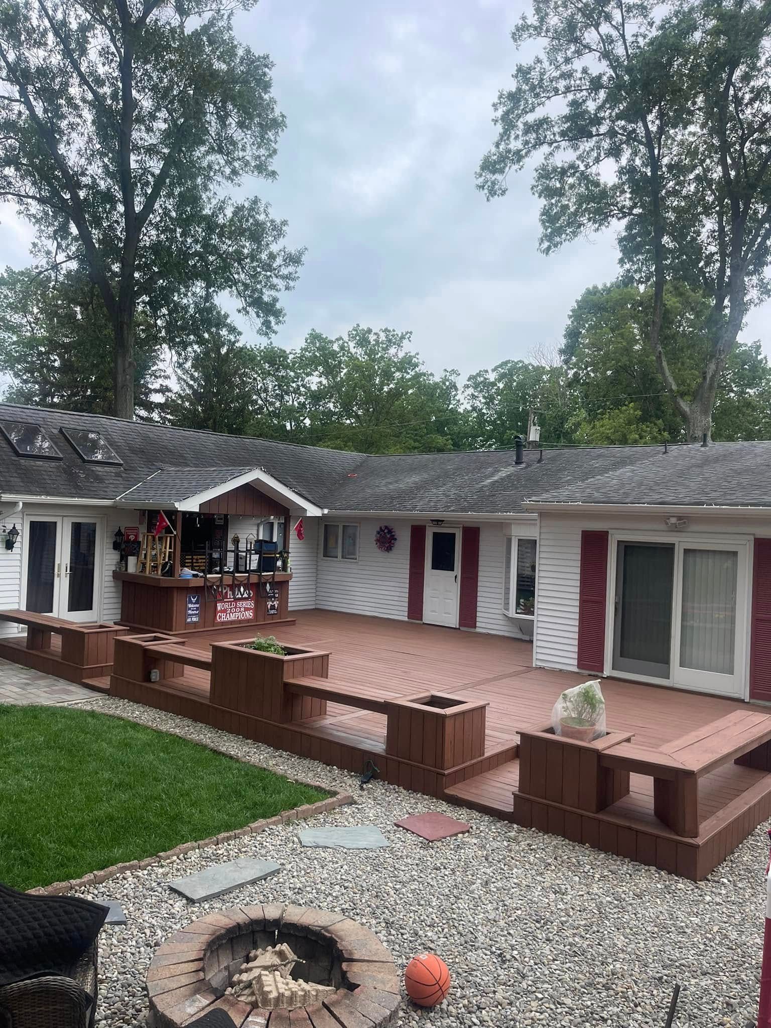 Backyard patio with brown deck seating, gravel fire pit, and a single-story house with white siding and pink shutters.
