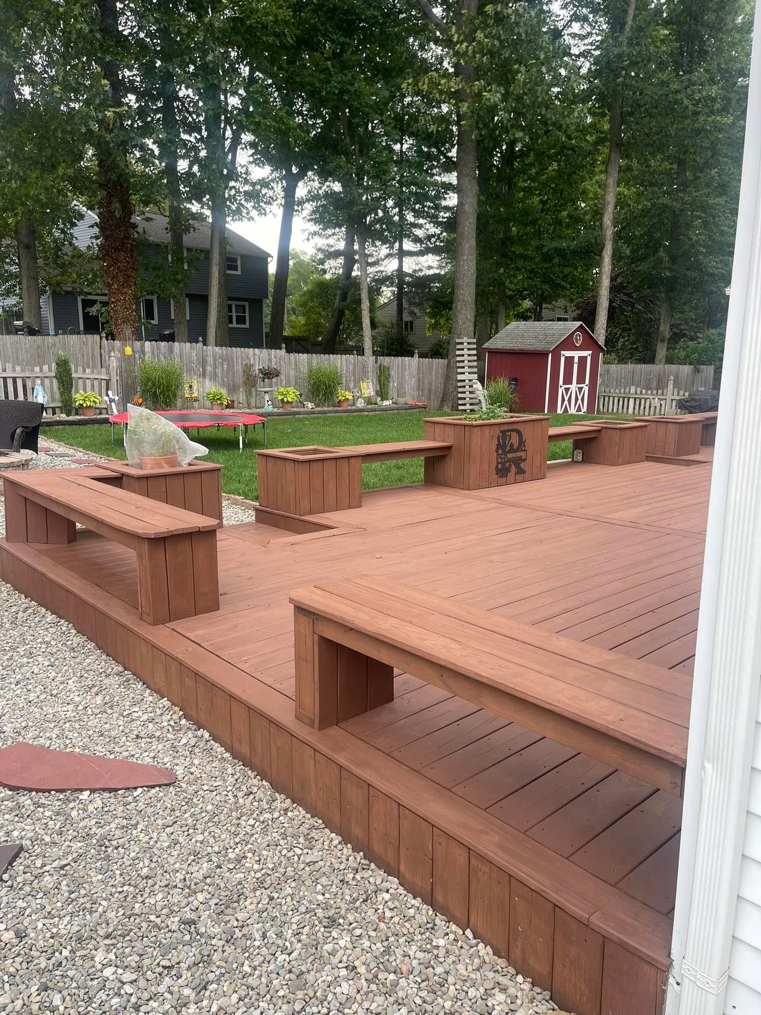Wooden deck seating area with benches, planters, gravel border, and trees in a landscaped courtyard