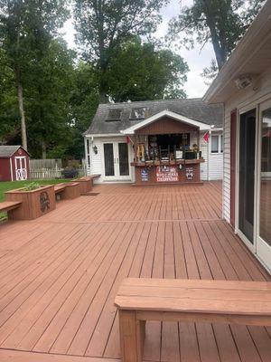 Wooden deck seating area outside a rustic white cabin under trees