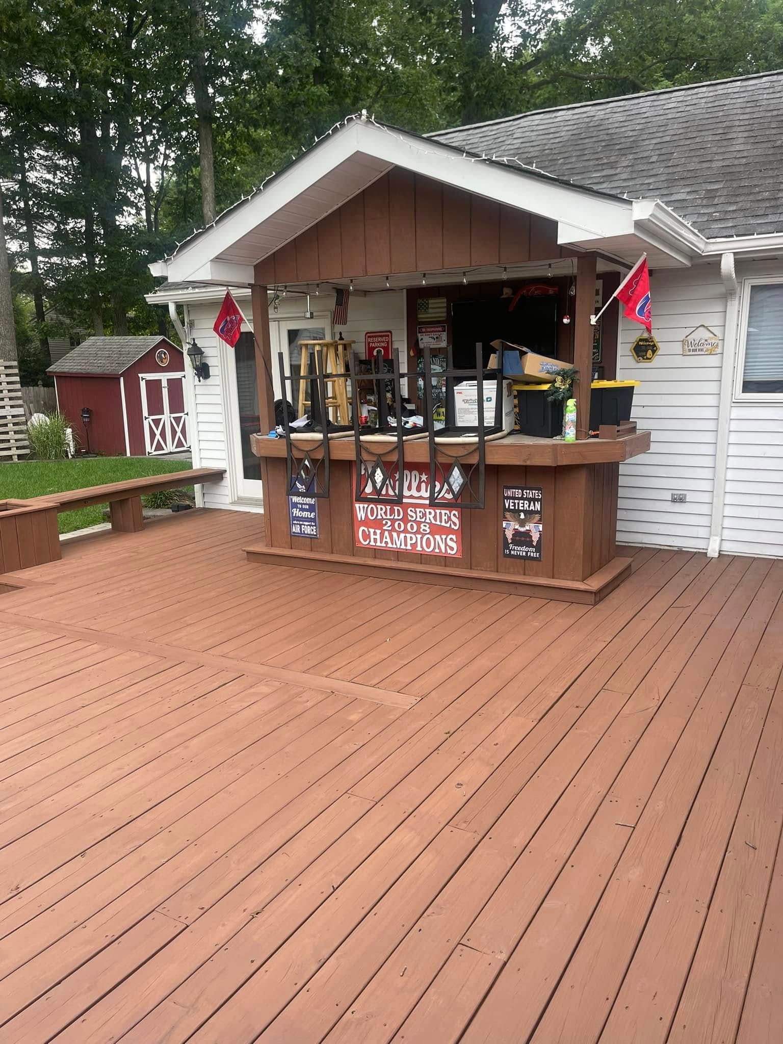 Wooden deck with a small rustic kiosk and flags outside a house, surrounded by trees.
