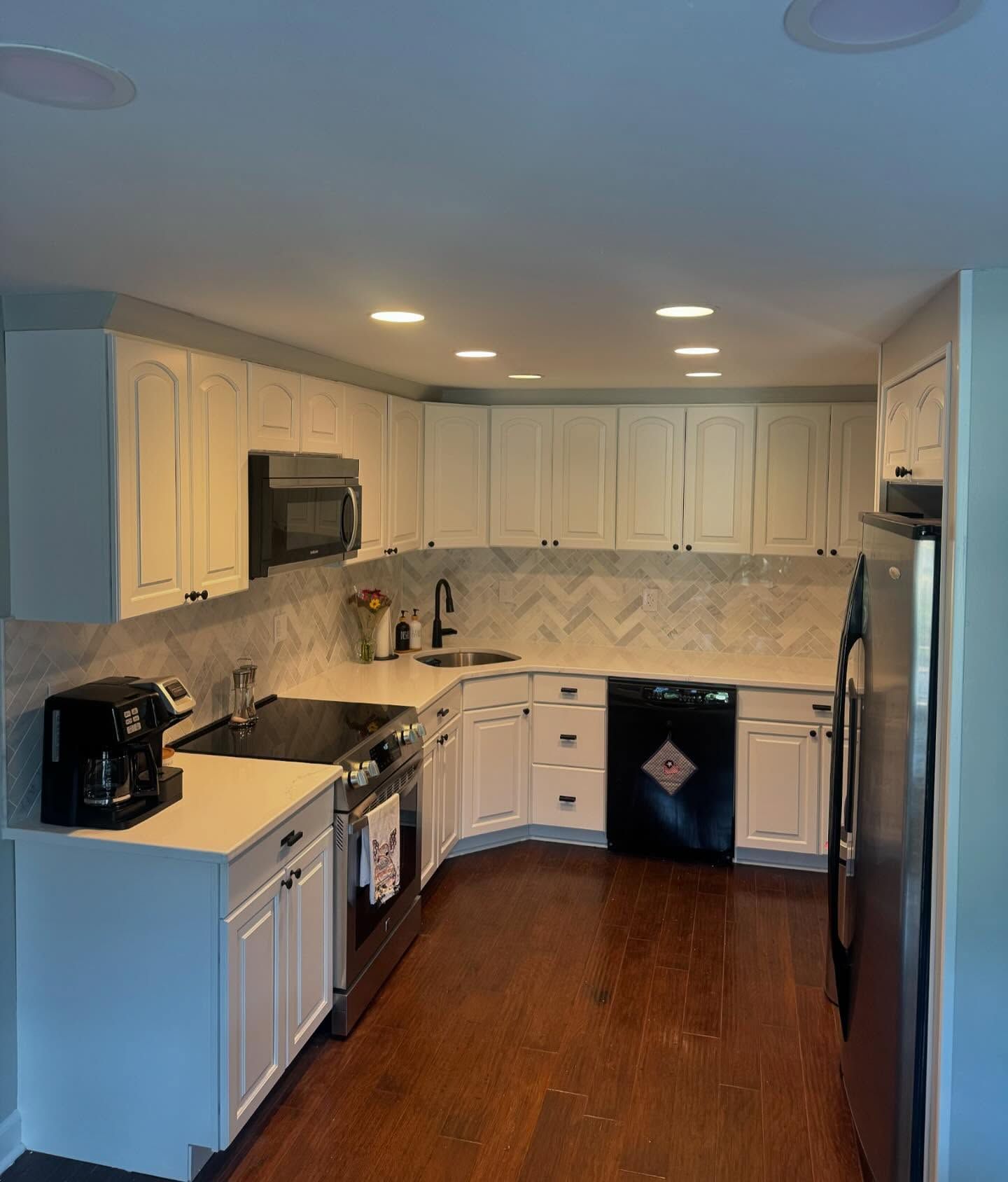 Bright white kitchen with wood floor, black appliances, and L-shaped white cabinets.