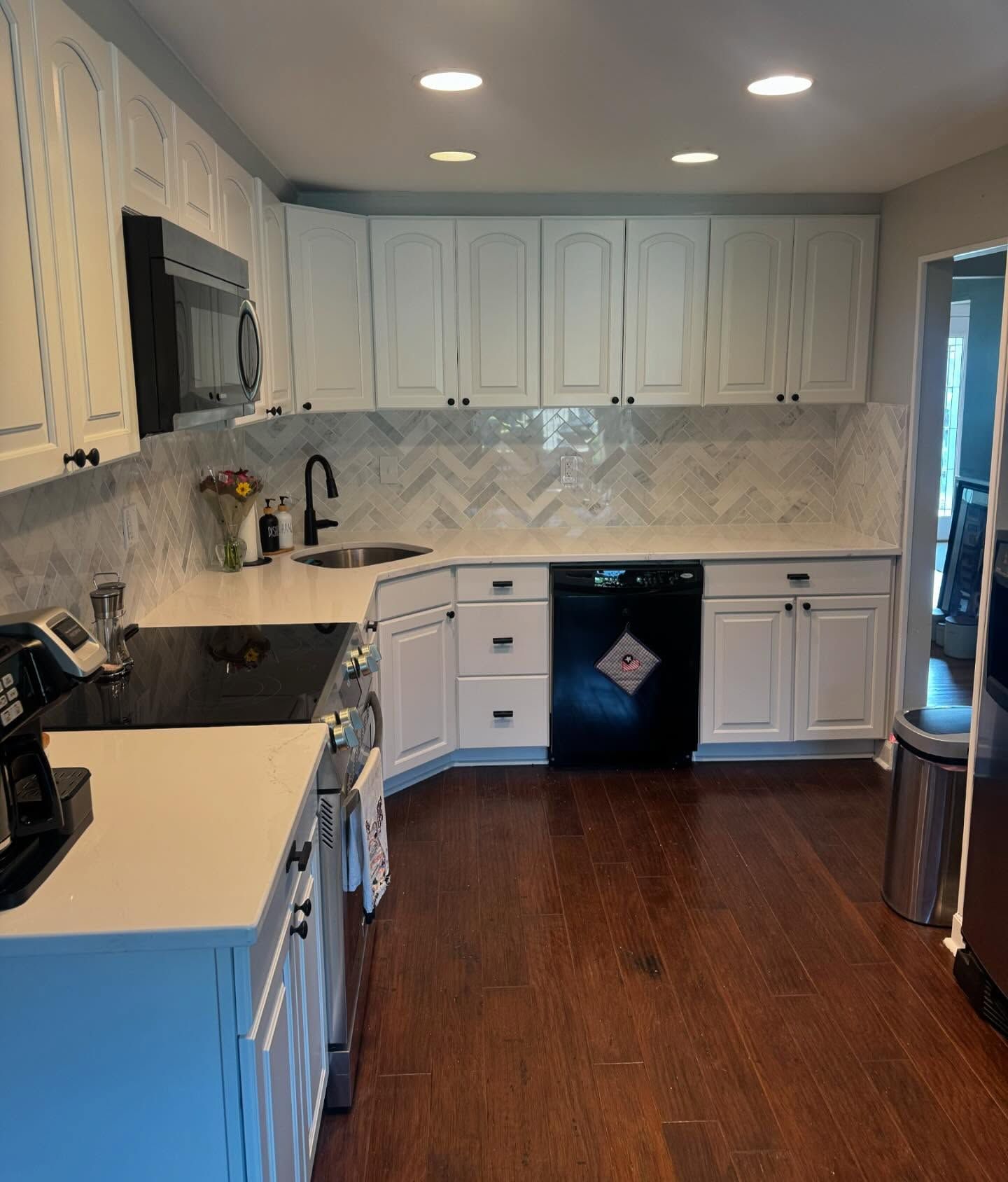 Bright white kitchen with black appliances, wood floor, and tiled backsplash