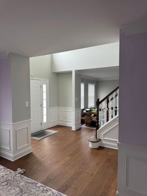 Bright foyer with hardwood floors, white walls, staircase, and bright entryway leading to a hallway