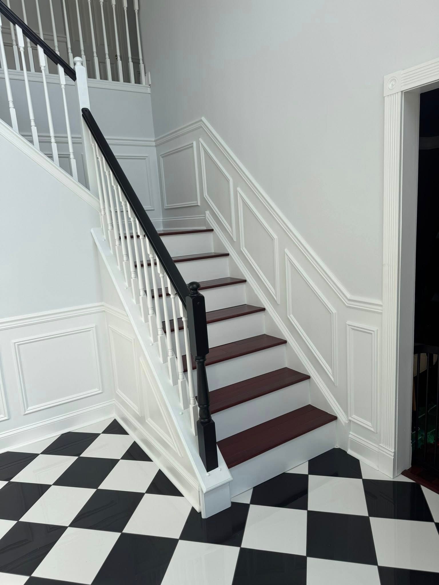 Staircase with white railing and dark steps beside a black-and-white checkered floor in a bright hallway