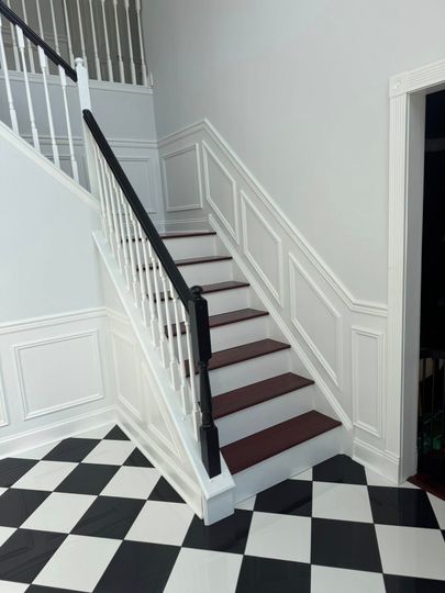 Staircase with white railings, dark steps, and black-and-white checkered floor in a bright interior