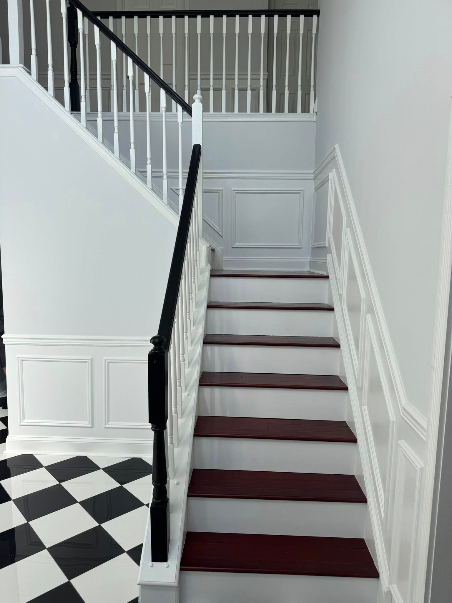Interior staircase with burgundy carpet, white walls, black banister, and black-and-white checkered floor