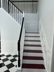 White staircase with dark railing and burgundy carpet, beside black-and-white checkered tile flooring.