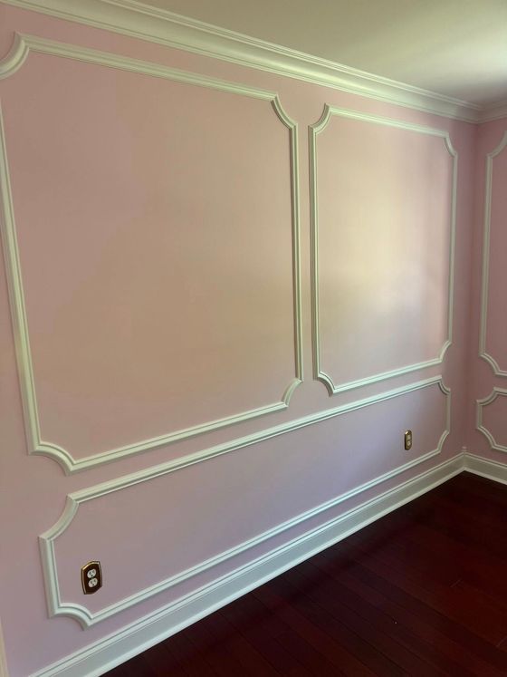 Pink room wall with white decorative molding and dark hardwood floor