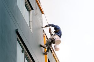 Person in a pink plaid shirt pointing up at a house window from below