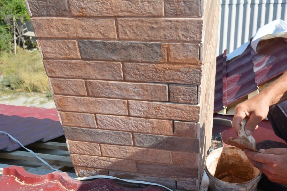A person is painting a brick chimney with a brush.