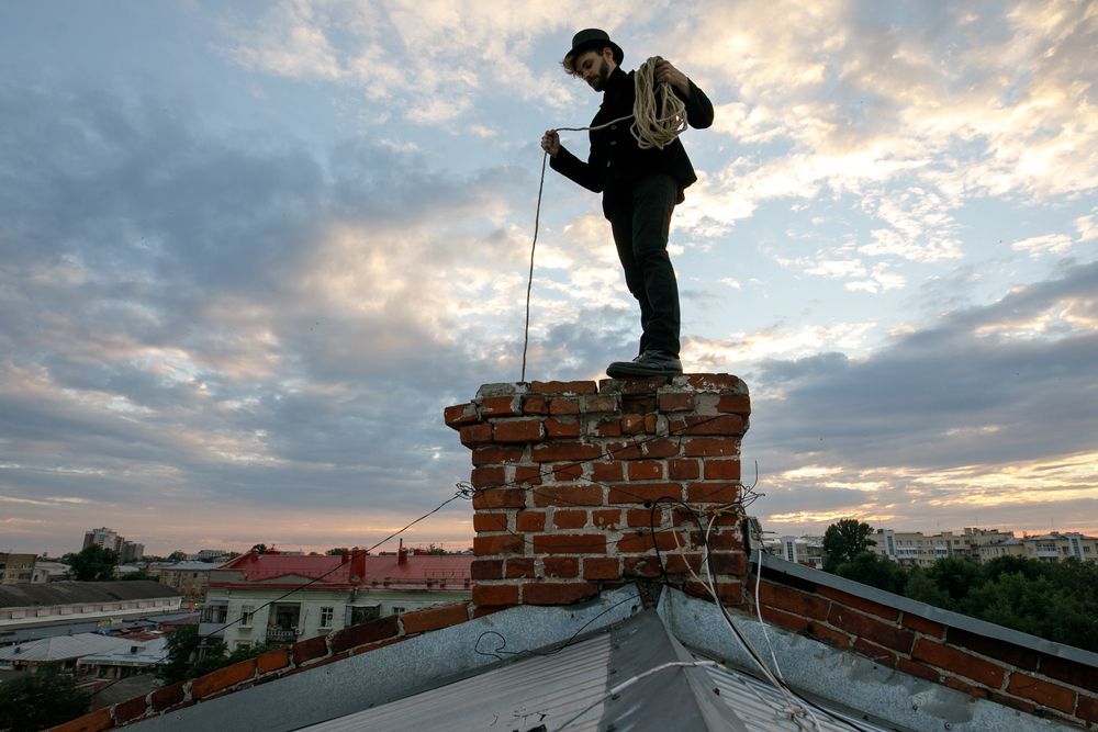 A man is standing on top of a brick chimney on a roof.