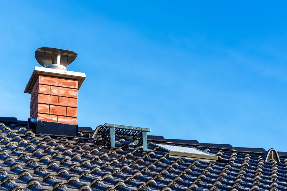 A brick chimney is sitting on top of a tiled roof.