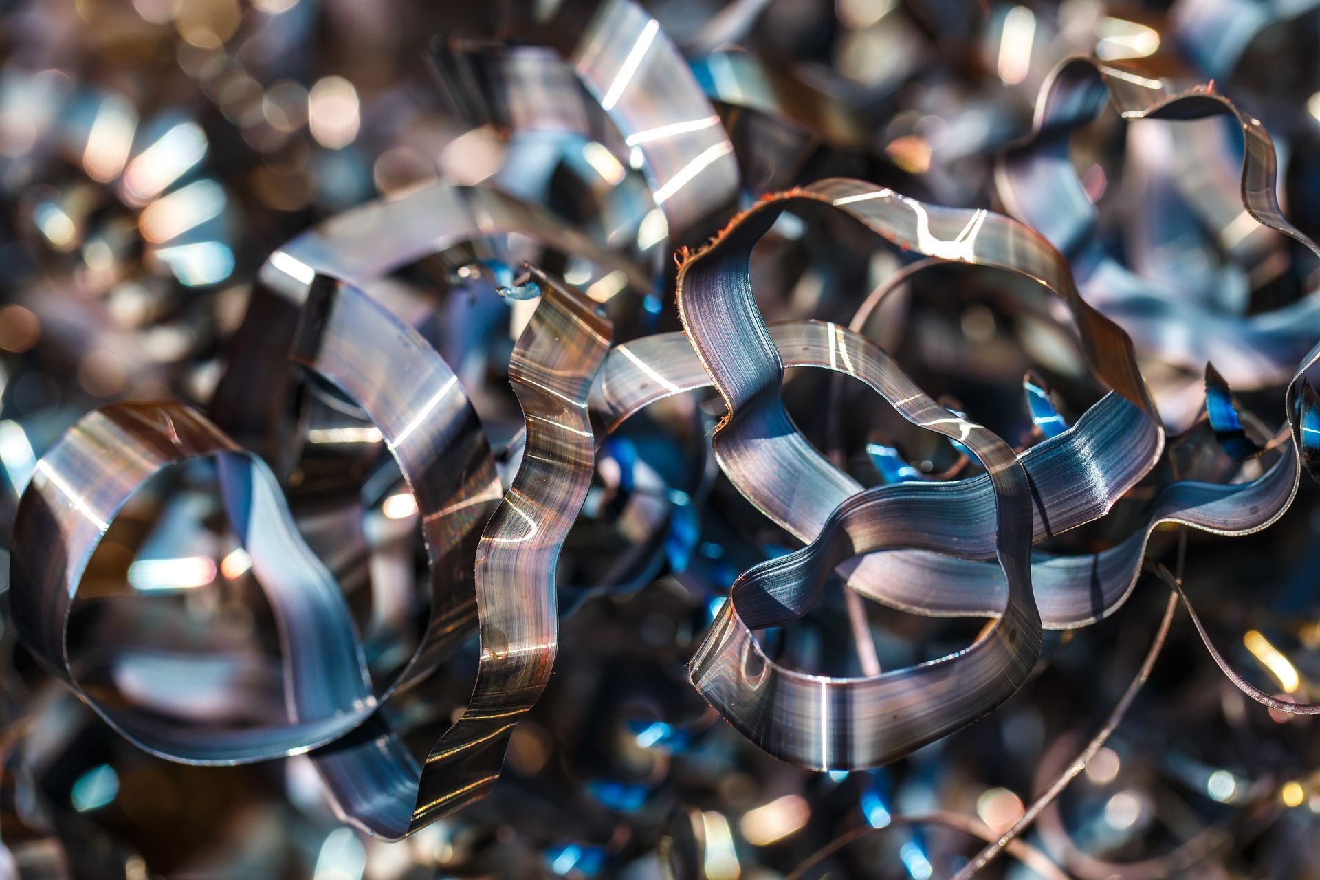 Curled strips of shiny metal shavings form a tangled pile ready for recycling. Curled strips of shiny metal shavings form a tangled pile ready for recycling.