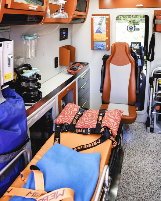 Barella ospedaliera con giubbotto blu da pronto soccorso e coperta piegati all'interno di un'ambulanza.